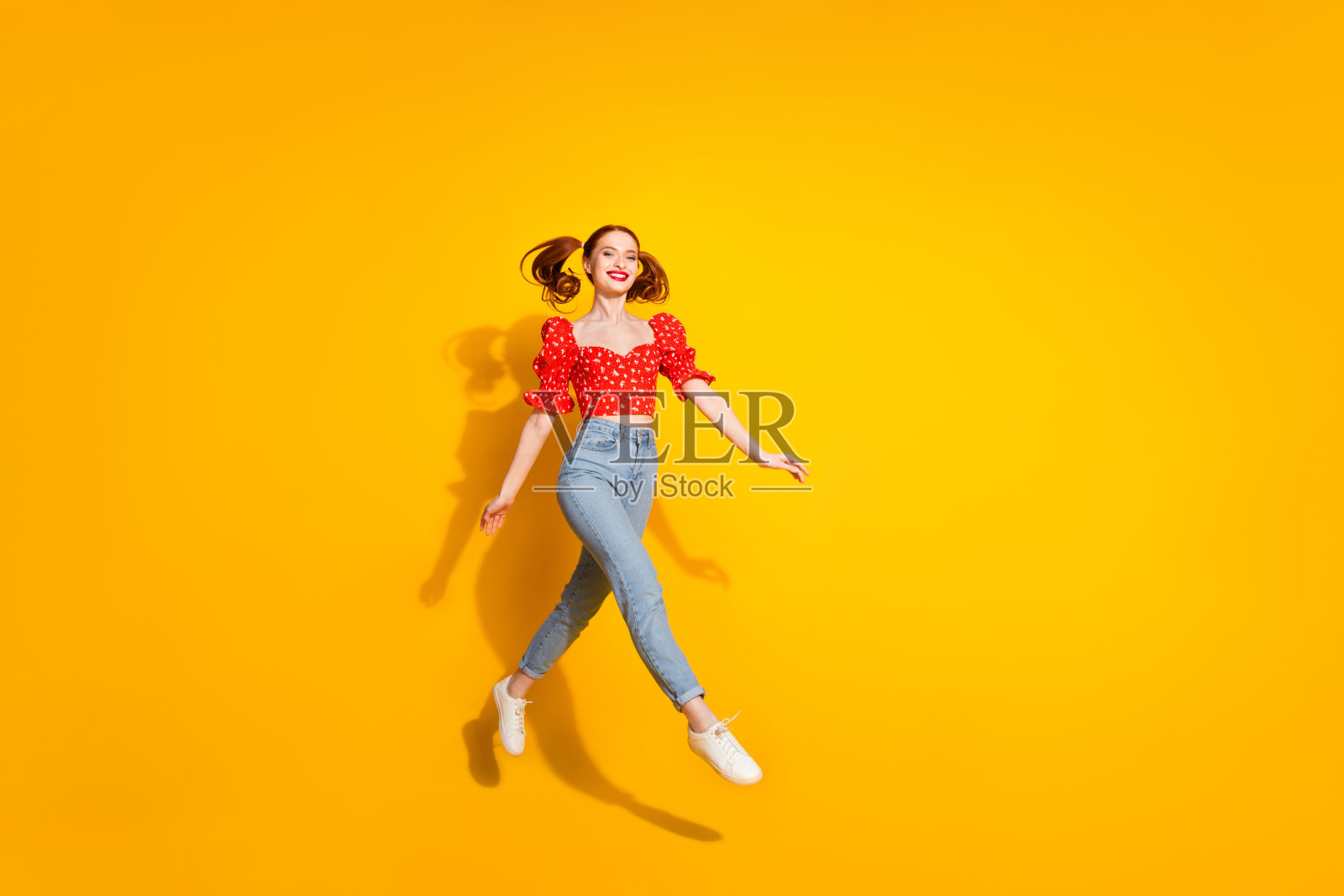 照片肖像年轻的红头发时髦积极的女孩穿着衬衫和牛仔裤跑跳无忧无虑孤立在黄色的背景照片摄影图片