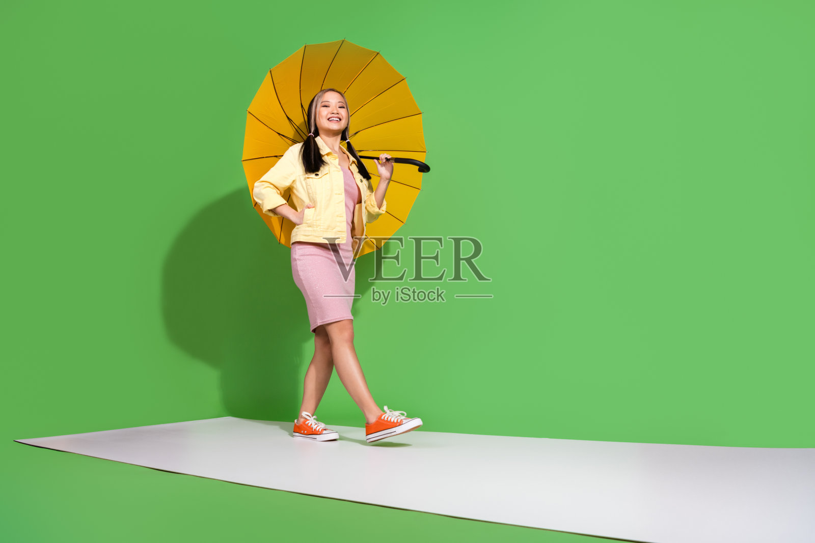 漂亮的年轻女子的全身肖像穿着夹克连衣裙走讲台伞孤立的绿色背景照片摄影图片