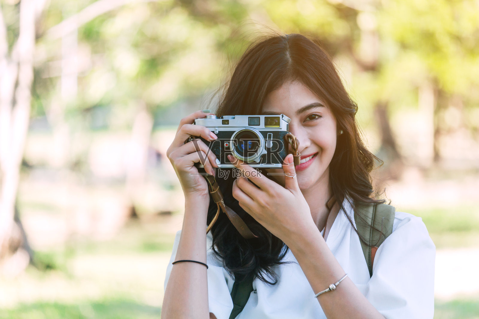 微笑的年轻女子站在公园用相机拍照的肖像照片摄影图片
