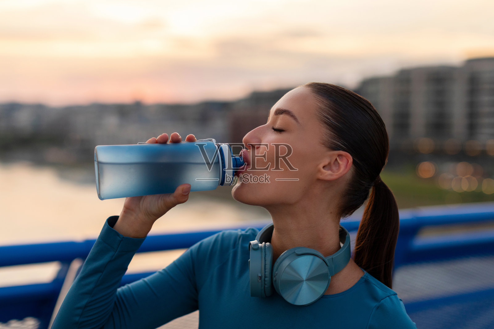 运动的欧洲妇女在跑步和喝水后休息，晚上锻炼时站在城市桥上照片摄影图片
