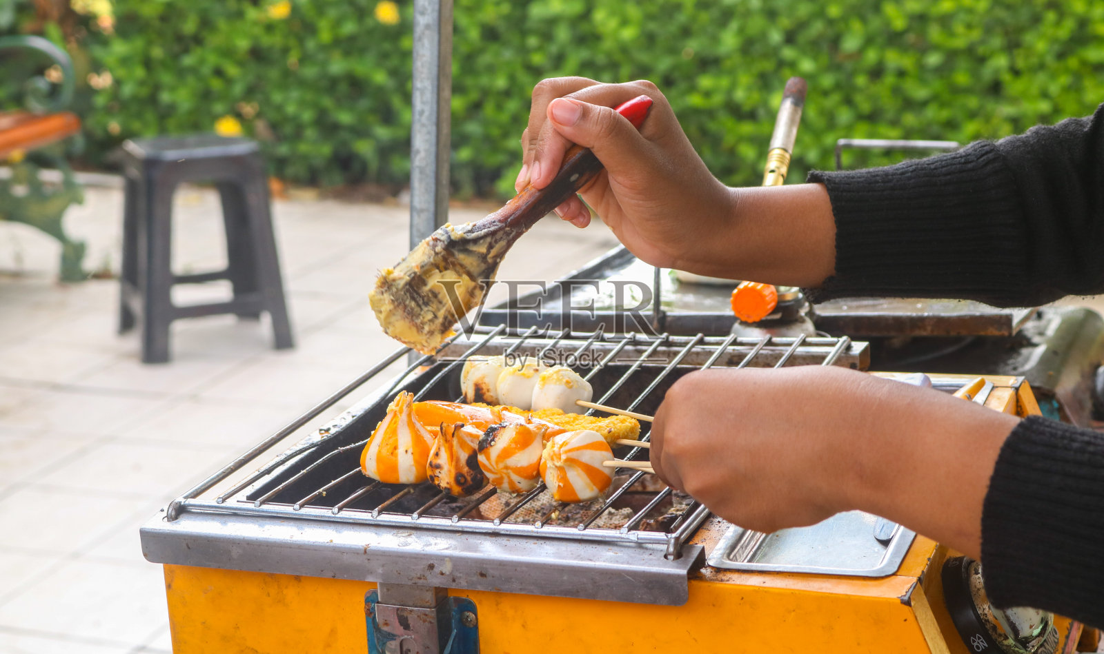 亚洲著名的街头小吃，烤肉丸、香肠、芝士饺子。在街边小吃摊上，一名妇女正在做沙茶肉丸和烤香肠照片摄影图片
