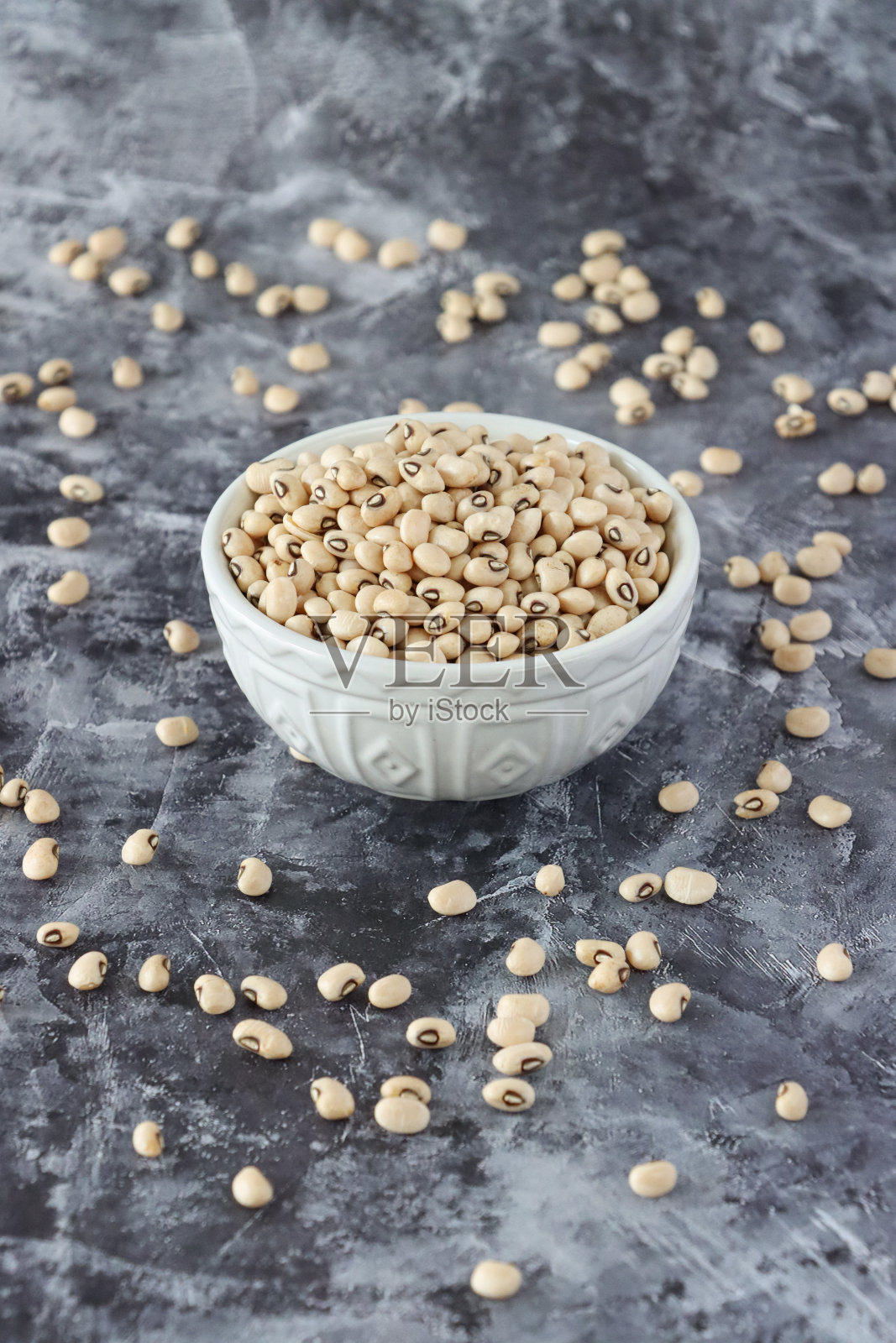 白色陶瓷碗里的黑眼豌豆，周围是散落的种子和豆类，花岗岩厨房台面背景下的健康食物照片摄影图片