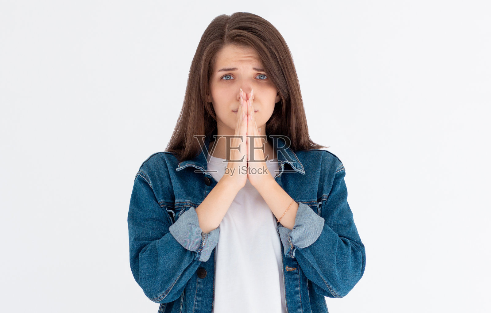 恳求女孩的肖像歪着头，噘起嘴唇，悲伤地看着镜头，做出祈祷的手势，寻求帮助和支持，乞求男朋友道歉，孤立在白色的墙上照片摄影图片