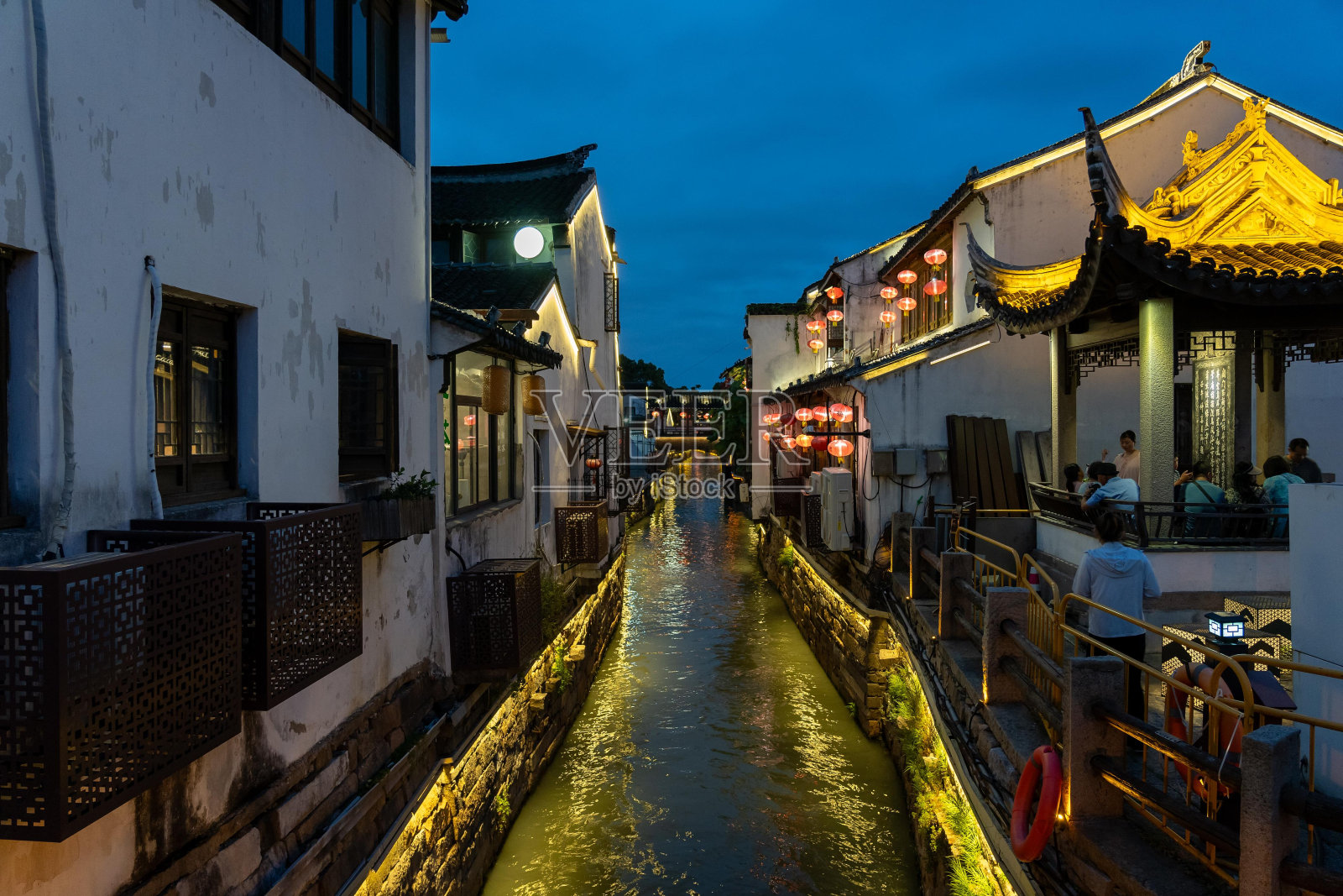 一条运河穿过中国苏州的中心地带，水面上挂着灯笼，灯火通明。运河沿岸的建筑古老而传统，细节复杂，屋顶华丽。照片摄影图片