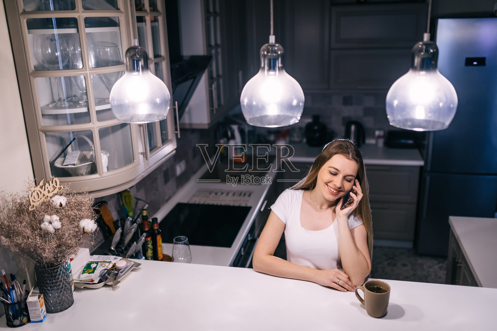 微笑的女士站在厨房一边用手机聊天。照片摄影图片