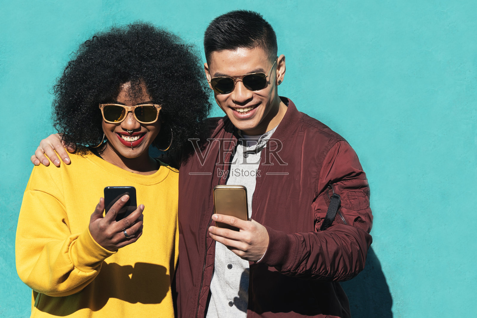 微笑的男人和女人站在绿松石墙前玩手机照片摄影图片
