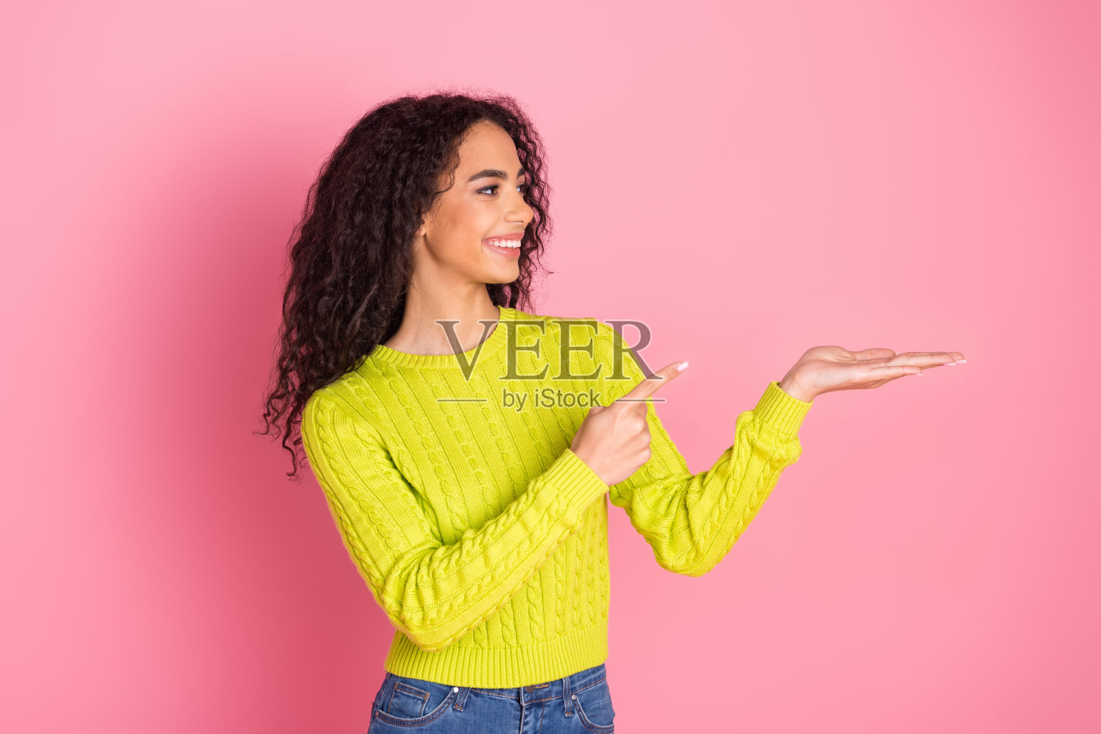 年轻的印度女孩穿着绿色套头衫的肖像照片，展示了粉红色背景上的新鲜产品信息照片摄影图片