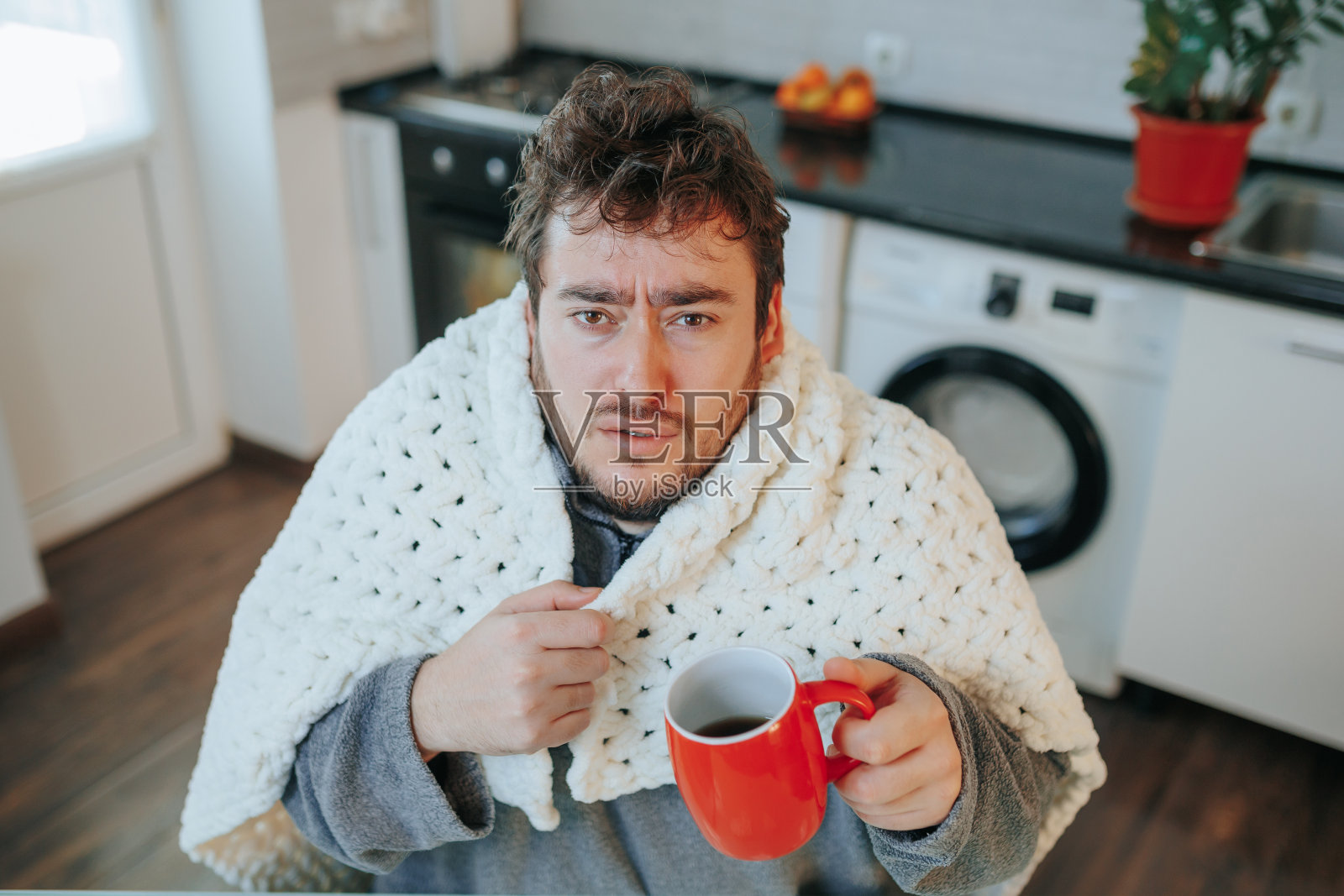 寒冷的特写:大胡子男子裹着羽绒被在家与寒冷作斗争照片摄影图片