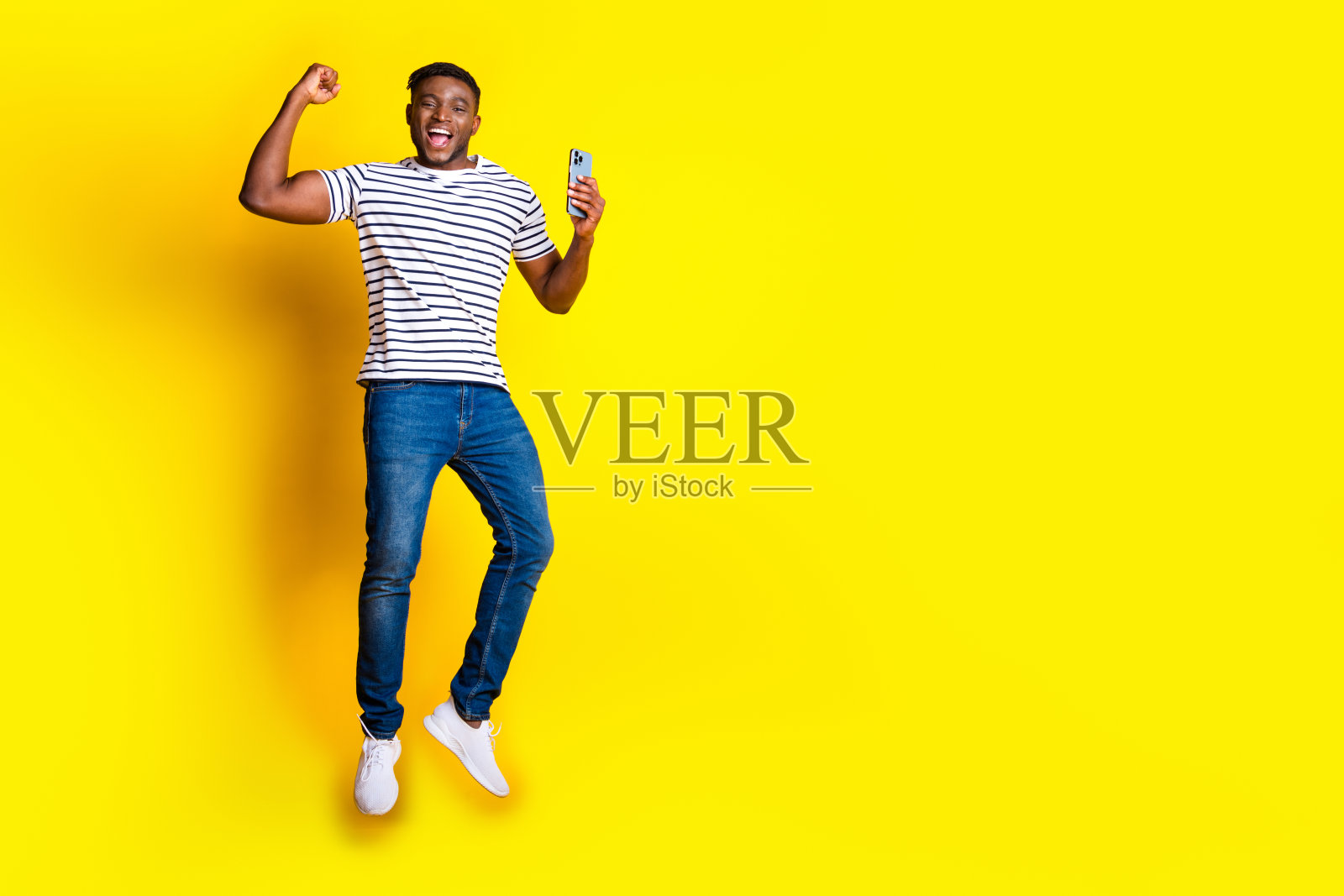 漂亮的年轻人的全身肖像跳智能手机穿t恤孤立在充满活力的黄色背景照片摄影图片