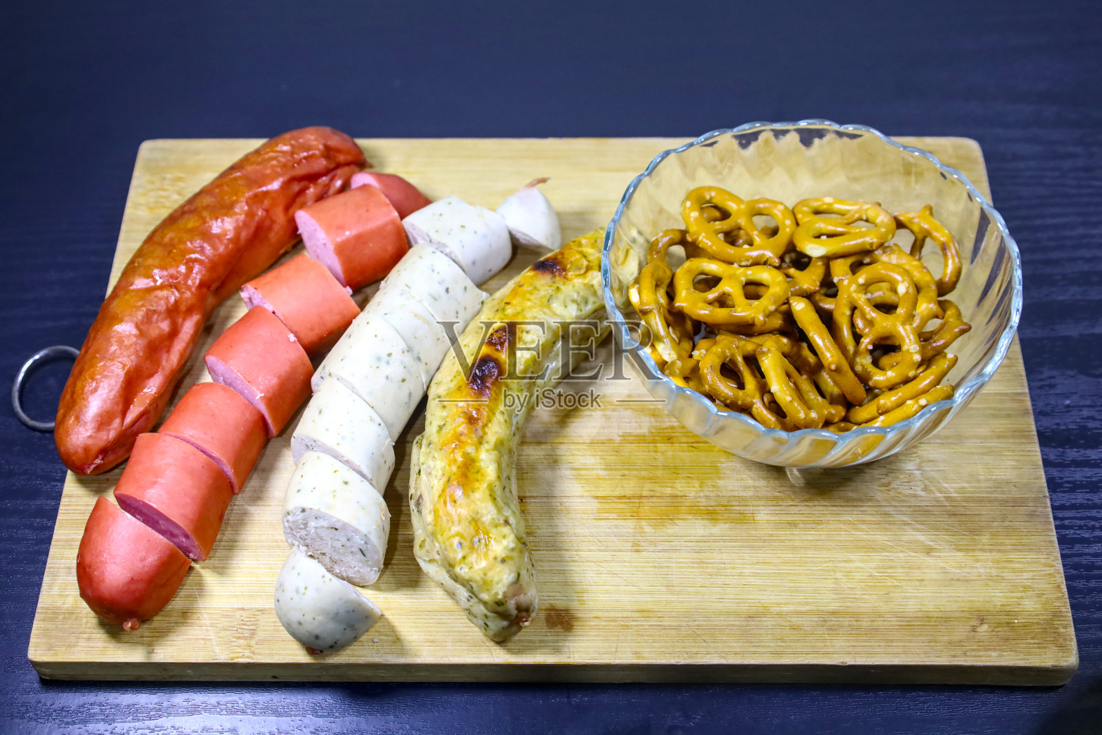 四根德国香肠(两根切片，两根整根)和椒盐脆饼放在木托盘上的水晶碗里照片摄影图片