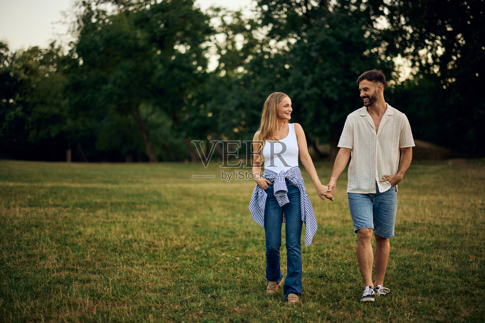 可爱的情侣穿过公园，手牵着手，看着对方。照片摄影图片
