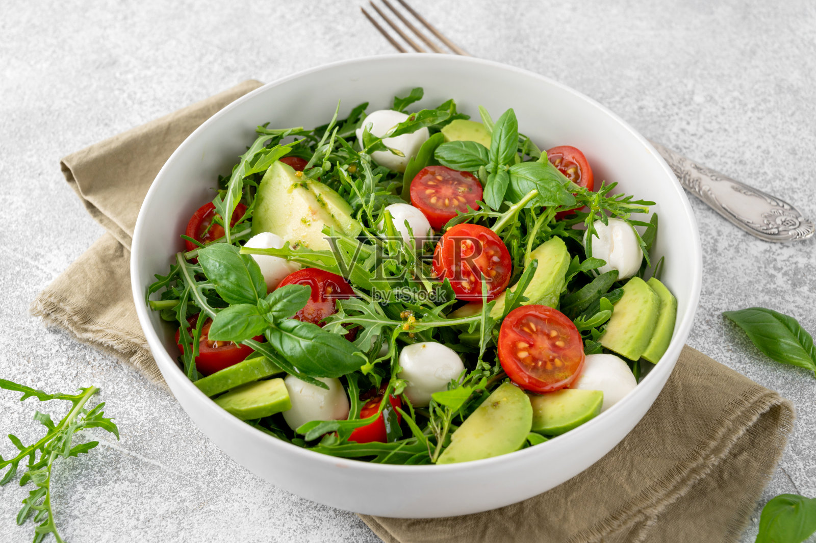 碗里有芝麻菜、马苏里拉奶酪、西红柿和鳄梨的新鲜沙拉。健康素菜。照片摄影图片