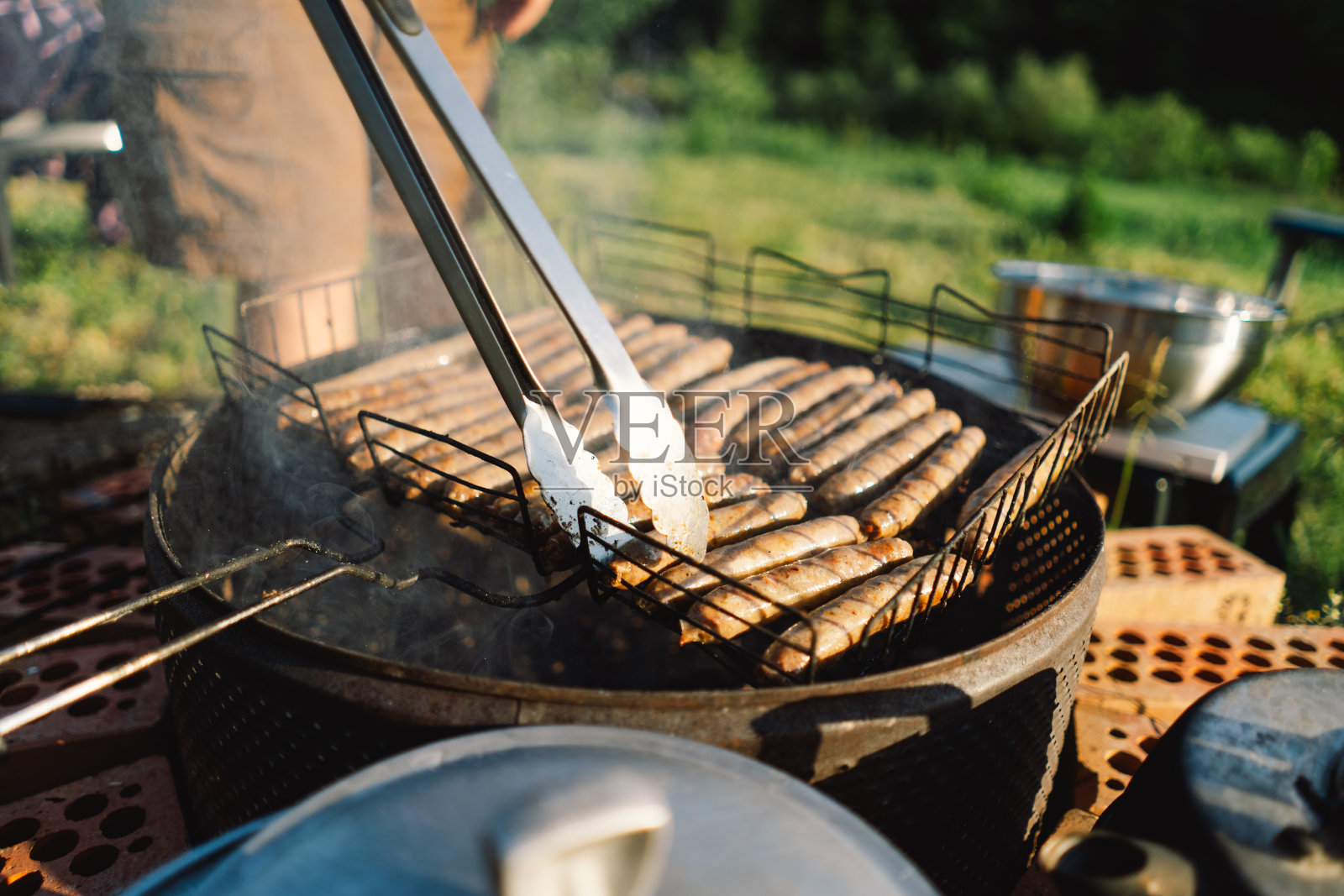 一名男子站在大自然中，在用砖块搭成的临时烤架上准备肉。照片摄影图片