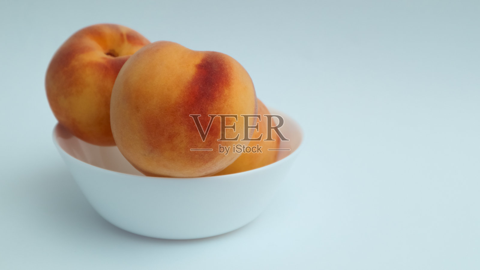 新鲜成熟的桃子放在白色的盘子里，白色的背景。维生素甜点。有机健康食品。照片摄影图片