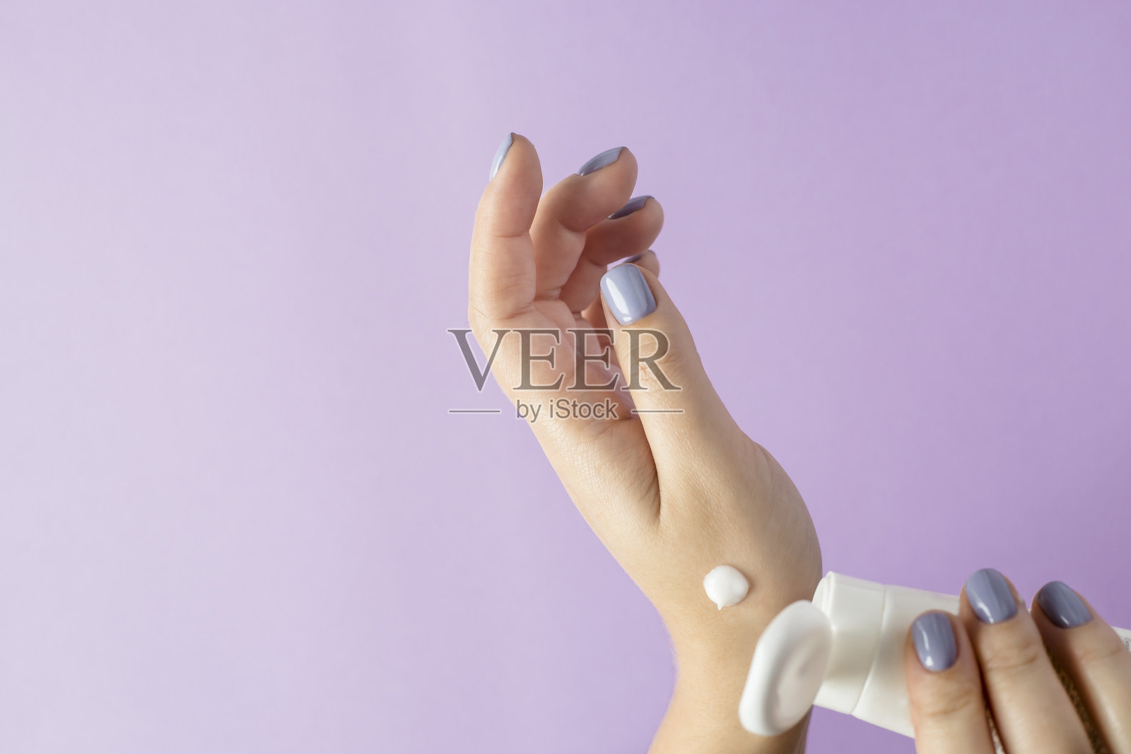 裁剪的手的女人拿着润肤霜对紫色的背景照片摄影图片