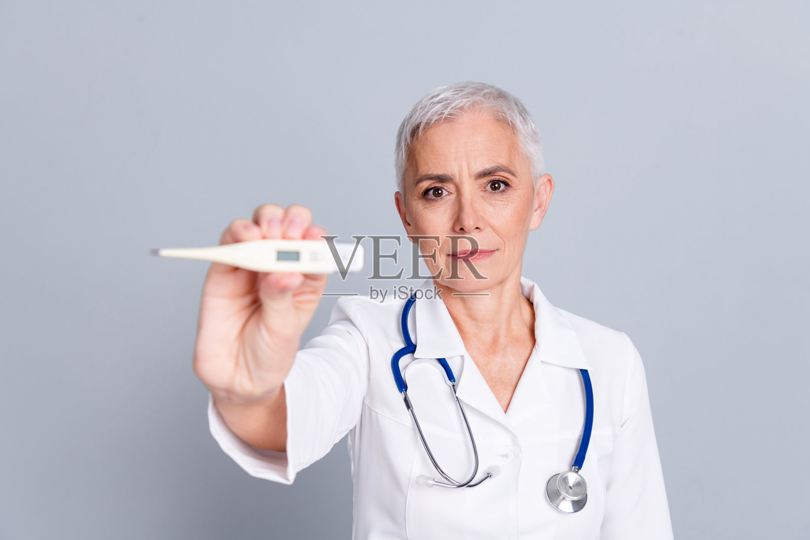 漂亮的退休女诊所专业医生的照片显示温度计穿着白色长袍制服孤立在灰色背景照片摄影图片