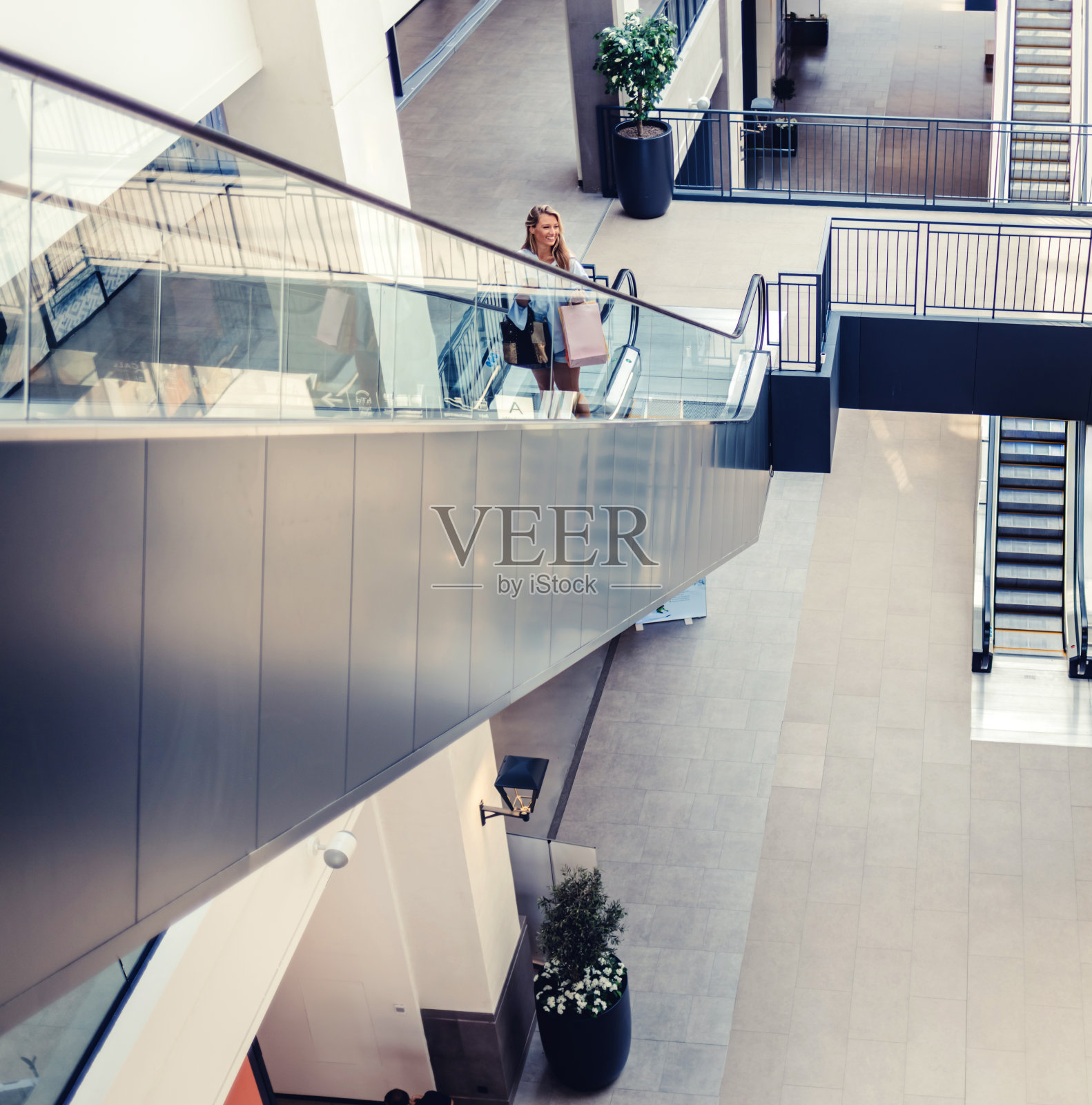 快乐的女商人在购物中心的自动扶梯上享受。一名拎着购物袋的妇女从购物中心的自动扶梯上走出来。照片摄影图片