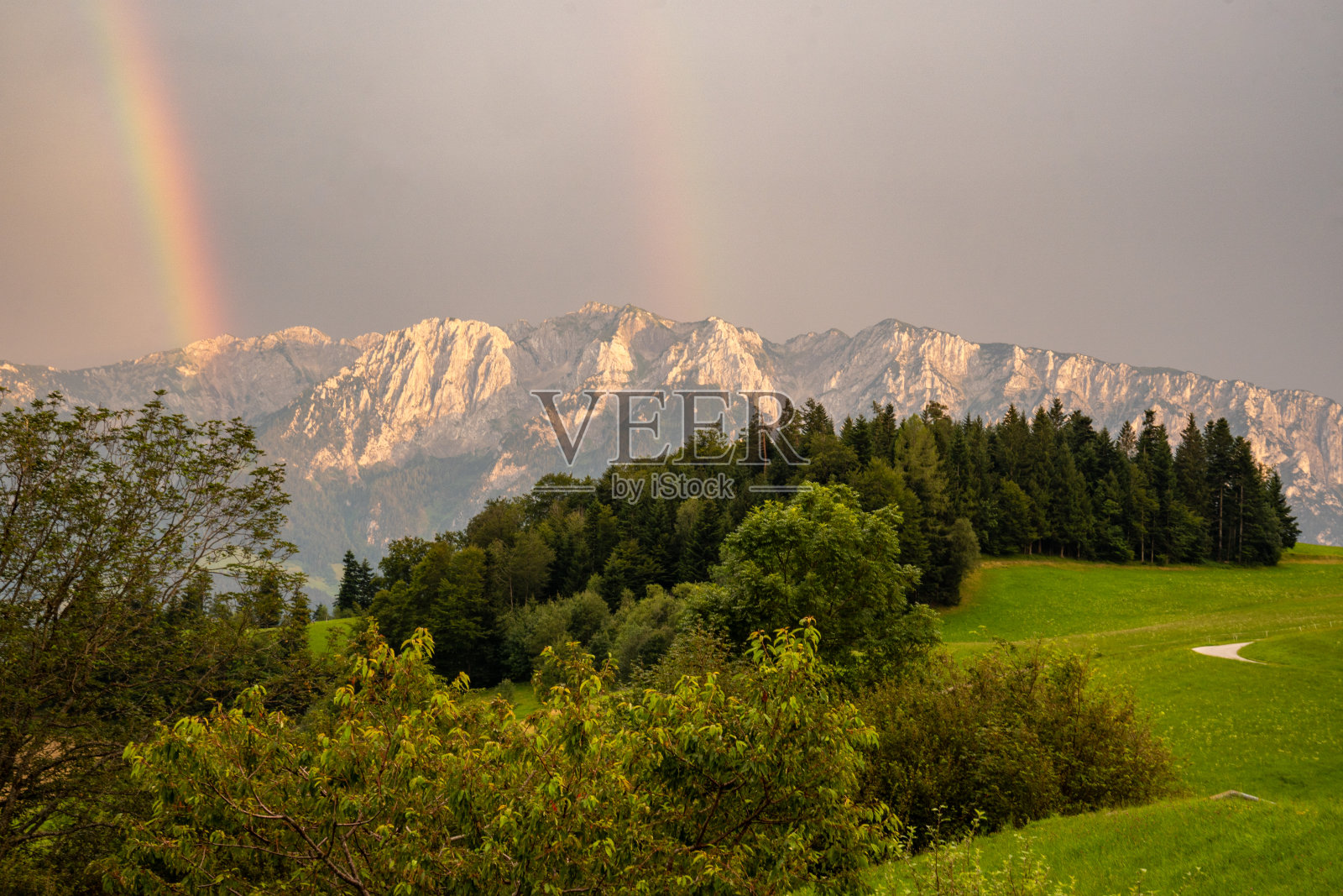 日落时分，奥地利蒂罗尔的扎赫默凯泽山脉出现双虹。森林和草地在前景照片摄影图片