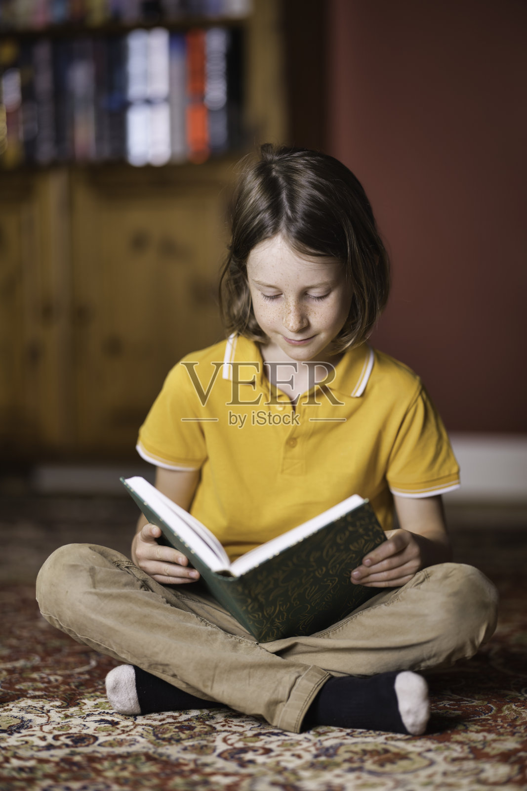 七岁的小男孩坐在地板上看书照片摄影图片