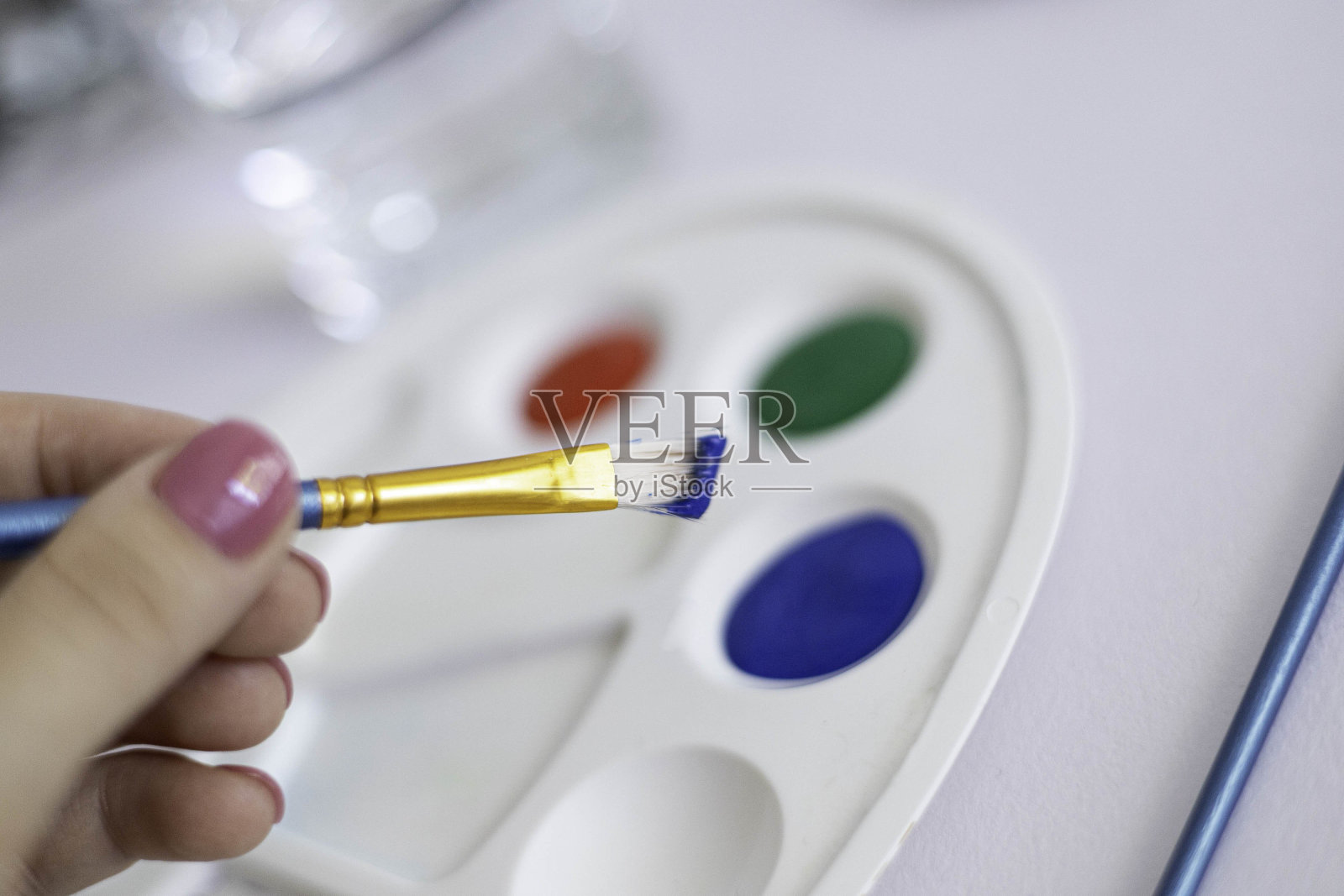 在这幅图中，一只手轻轻地拿着一个蓝色手柄的刷子，在一个充满鲜艳色彩的调色板上。调色板以红、绿、蓝三色为特色，随时准备进行创造性的探索。这个场景通过展示艺术过程来表达对艺术过程的期待照片摄影图片