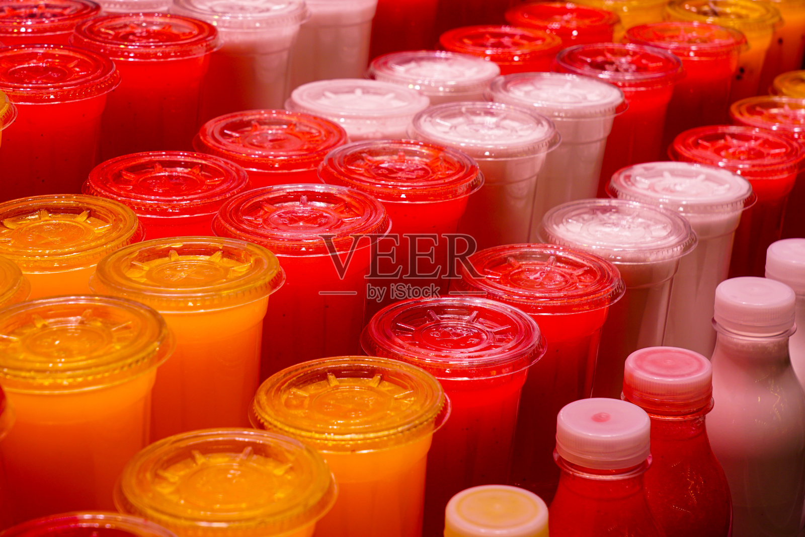 在市场摊位上，用透明塑料杯榨出的各种鲜榨果汁照片摄影图片