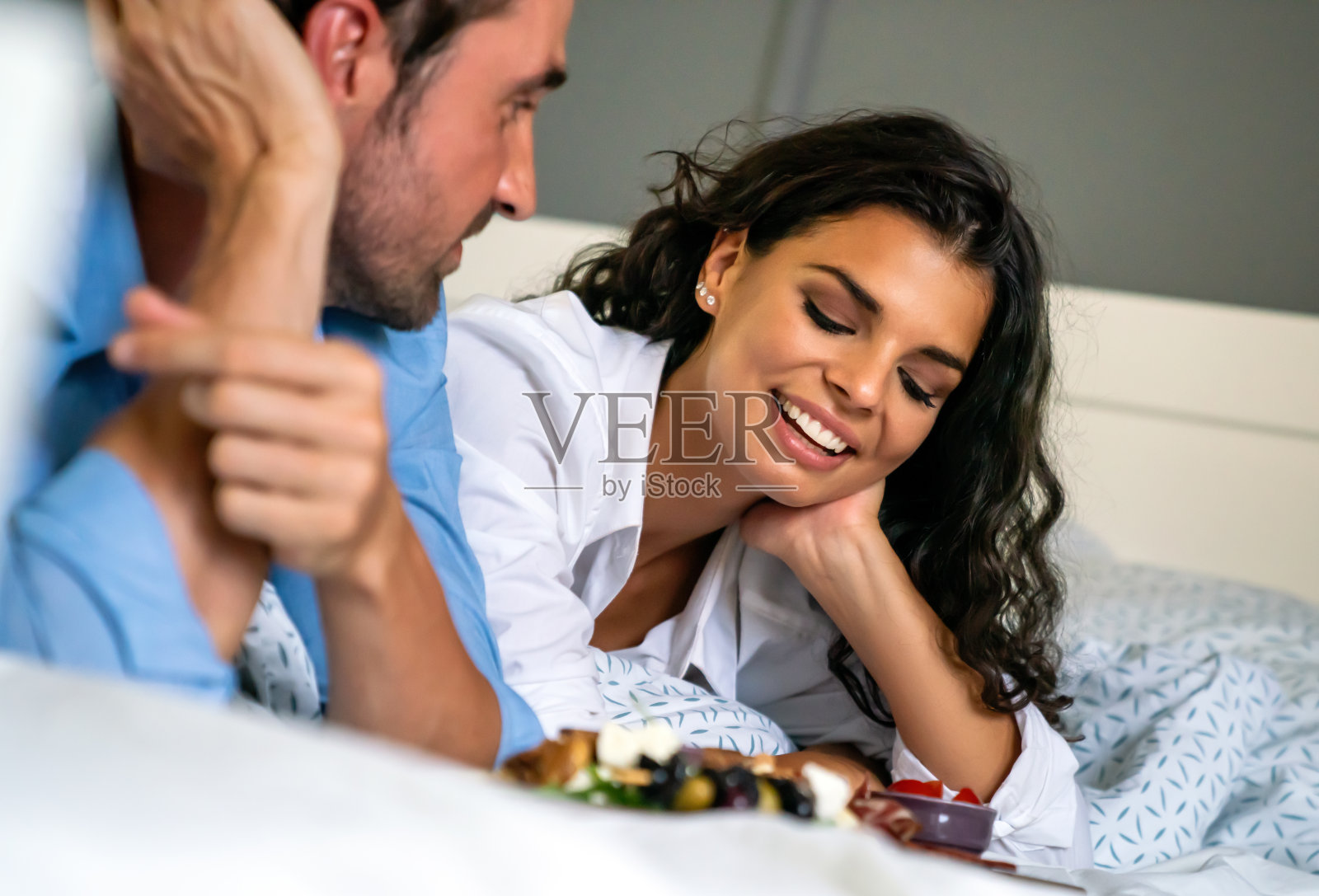 幸福的年轻夫妇在床上吃着健康的沙拉。多种族相爱的人在家里享受周末。照片摄影图片