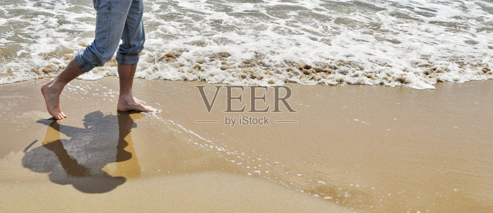 阳光明媚的日子里，男人在海滩上散步的低剖面照片摄影图片