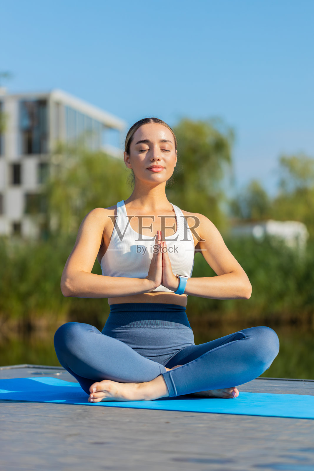 夏日里，一位白种女子坐在公园池塘边的垫子上，以莲花的姿势放松照片摄影图片