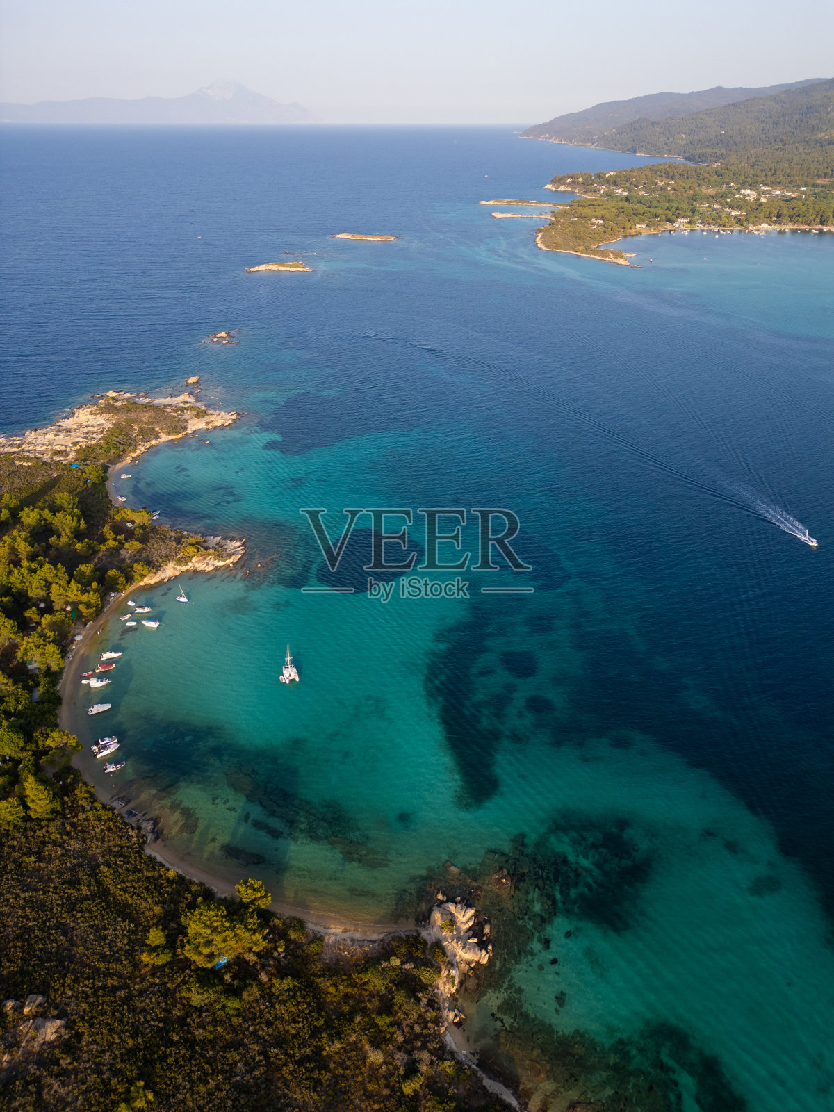 鸟瞰希腊西托尼亚半岛上的一座岛屿，海滩和岩石环绕在清澈的海水中。游艇和船只停泊在碧绿的海水中。附近的小岛和暗礁可见照片摄影图片