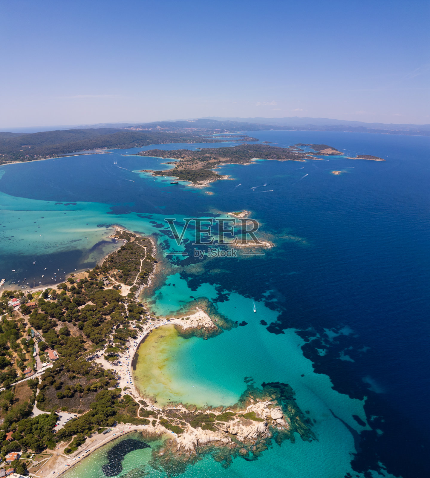 鸟瞰希腊西托尼亚半岛上的一座岛屿，海滩和岩石环绕在清澈的海水中。游艇和船只停泊在碧绿的海水中。附近的小岛和暗礁可见照片摄影图片