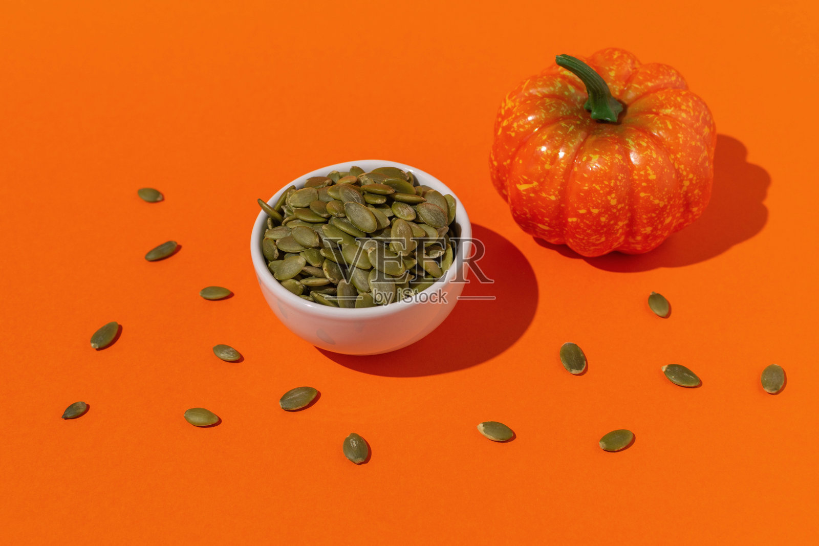 南瓜种子在白色碗与迷你南瓜在橙色背景照片摄影图片