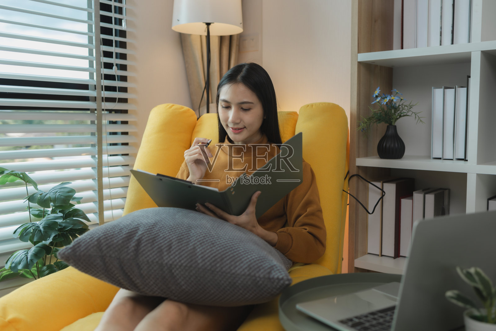 一个亚洲女人正坐在客厅的沙发上，查看她周末带回家的工作。她利用空闲时间仔细检查她的工作和文件。照片摄影图片