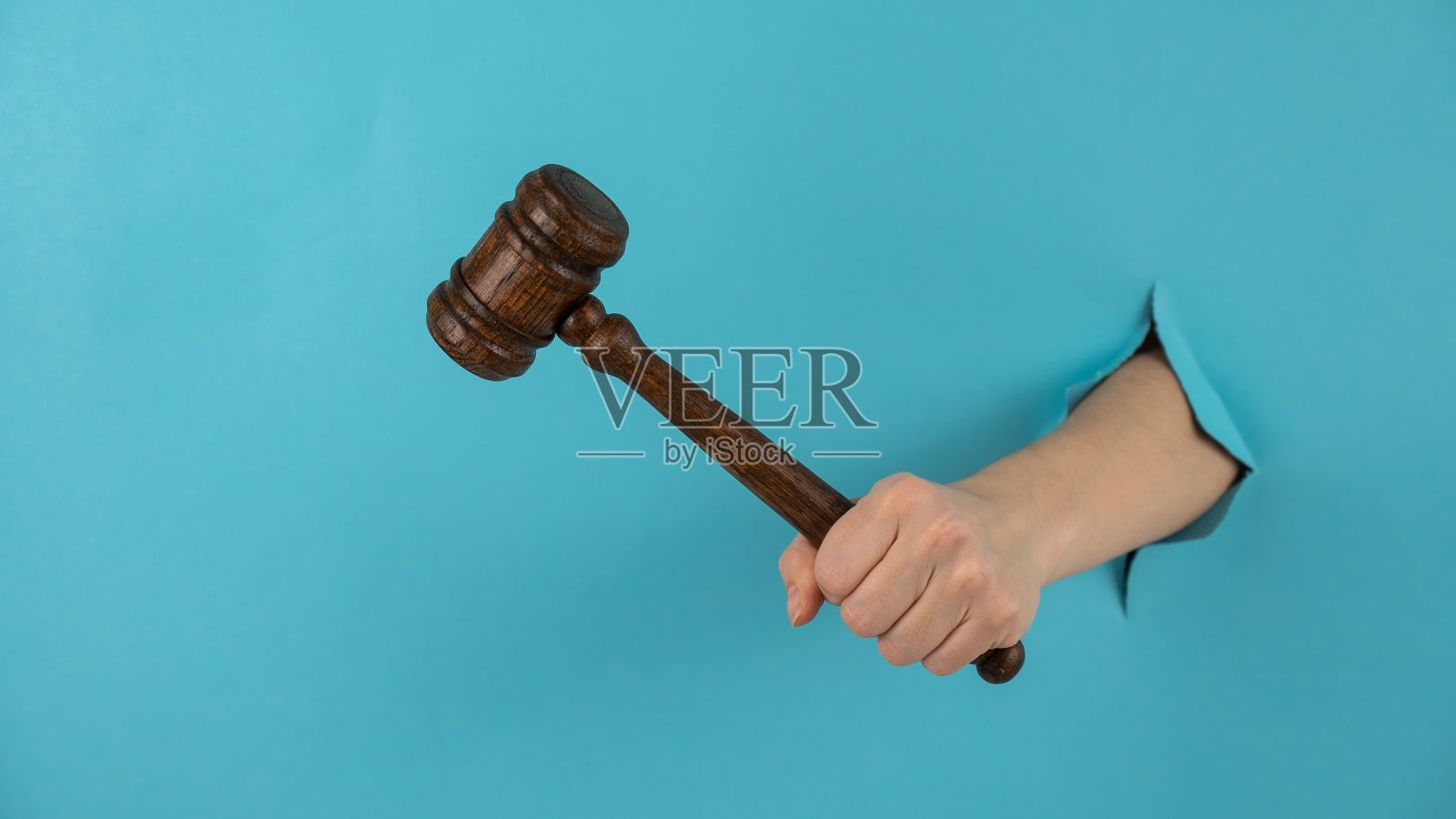 女人手拿着木制法槌，从蓝色背景的洞里伸出。照片摄影图片