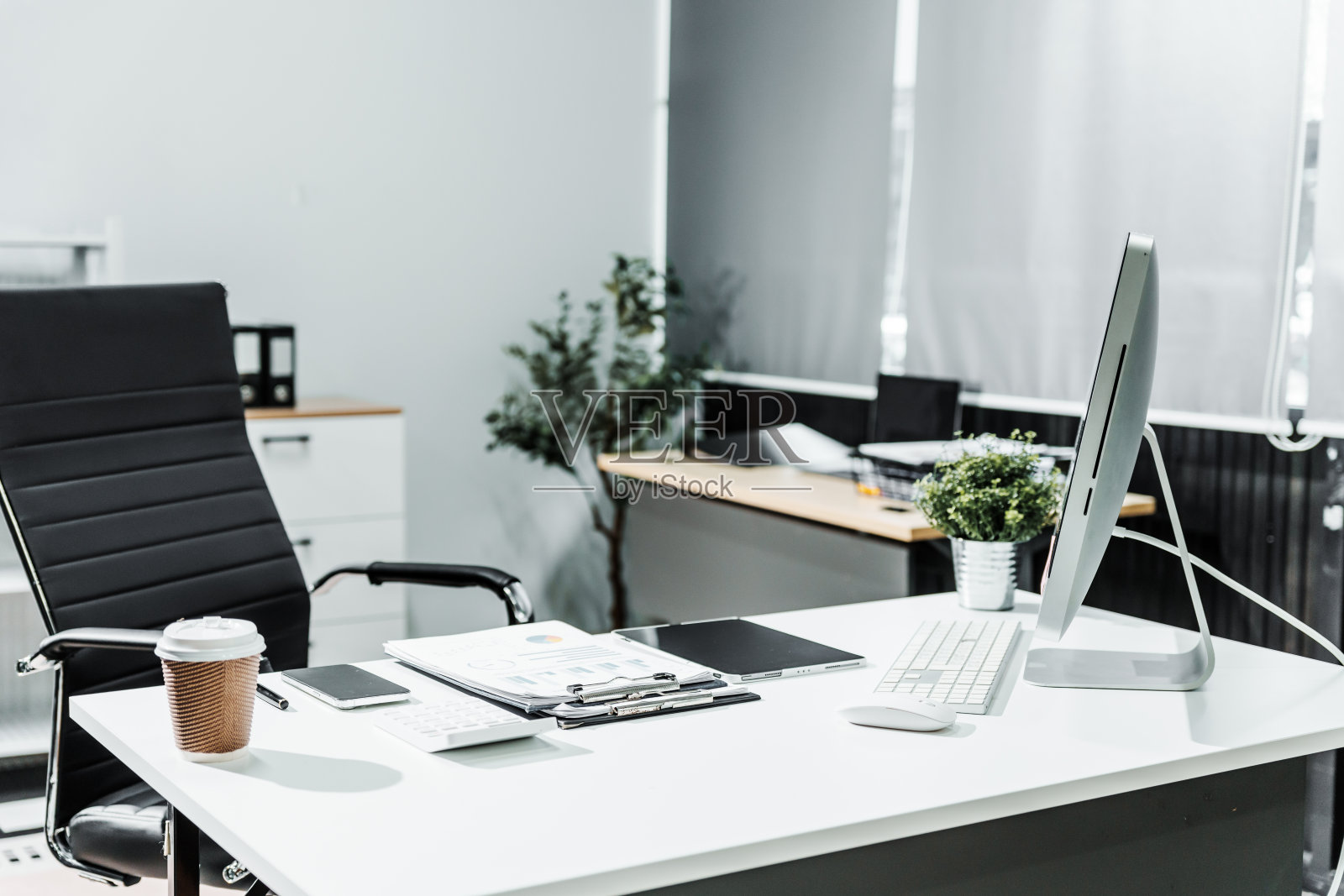 一个现代的，白色的商务办公室，有木桌，计算器，台式电脑和黑色皮椅。行政办公室为办公室主任提供私人办公家具。照片摄影图片