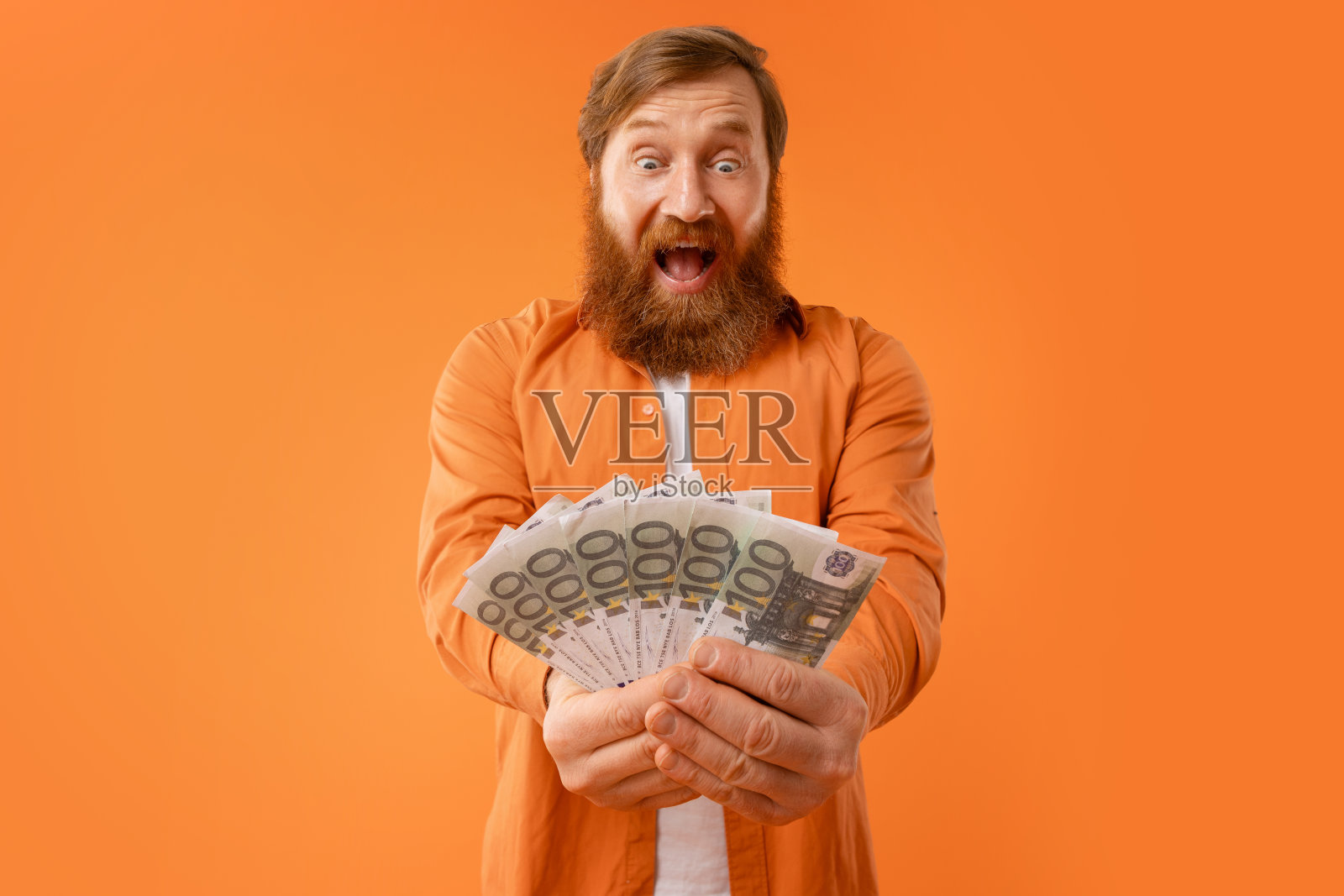 男子拿着橙色背景的欧元钞票，高兴地大喊照片摄影图片