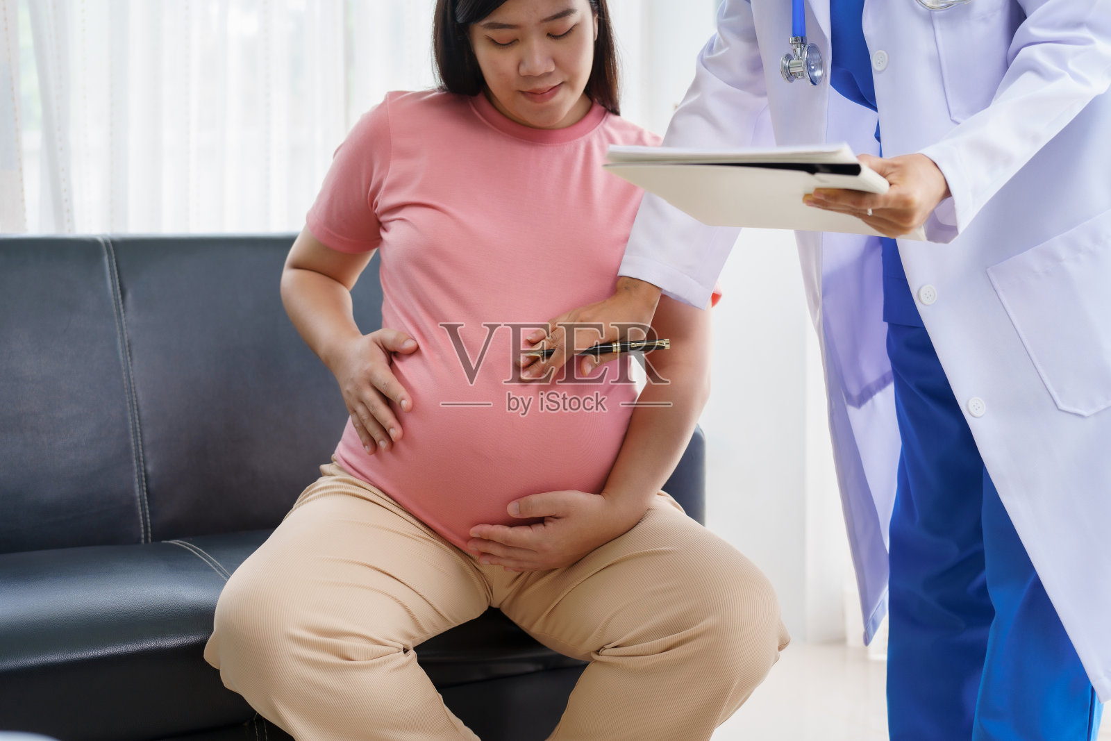 诊所里，孕妇坐在沙发上，医生检查她的腹部并查看超声波结果，握着她的手给予鼓励和关怀照片摄影图片