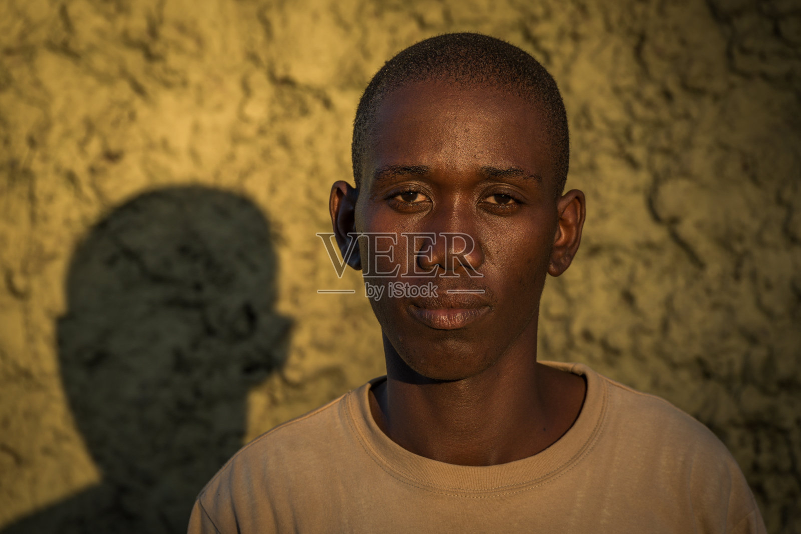 阳光灿烂的日子里，严肃的年轻人靠墙站着的肖像照片摄影图片