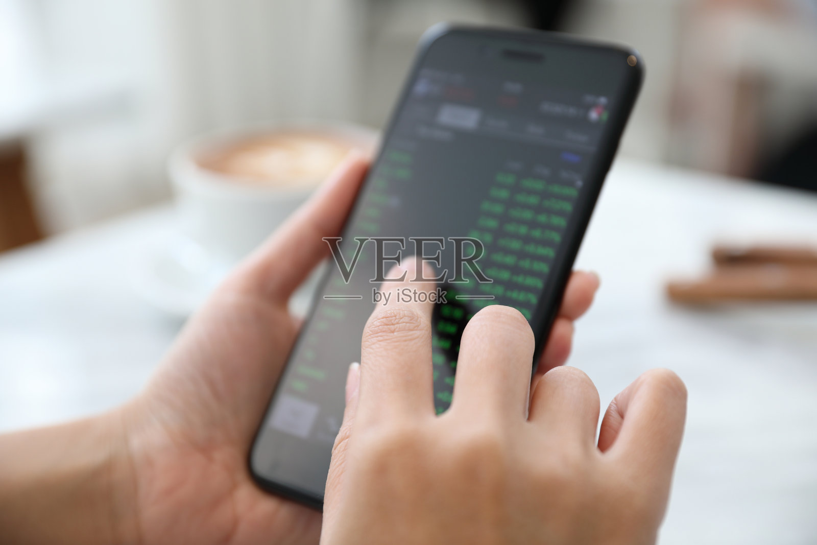 特写裁剪的手拿着手机与屏幕上的图表在桌子上照片摄影图片