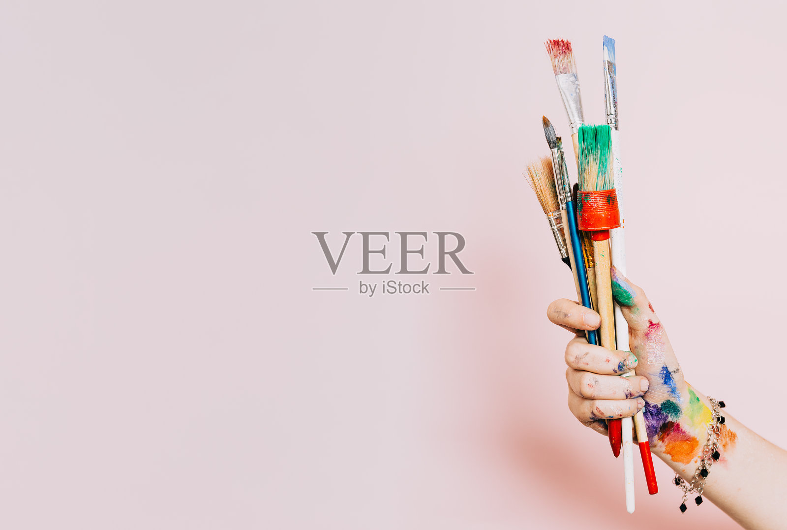 创造性的背景。女艺术家手握彩色画笔。油漆和刷背景。艺术课，艺术学校。粉红色的艺术背景，复制空间。一套脏刷子。照片摄影图片