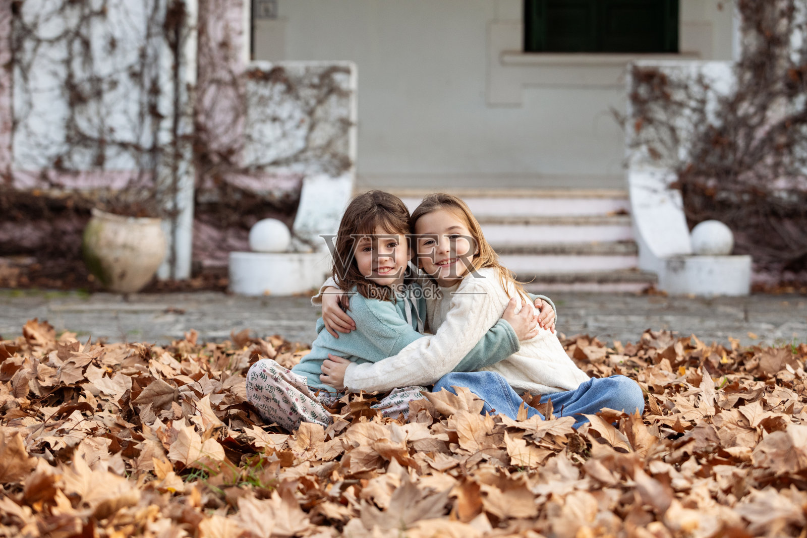 两个女孩坐在秋天的干树叶上拥抱照片摄影图片