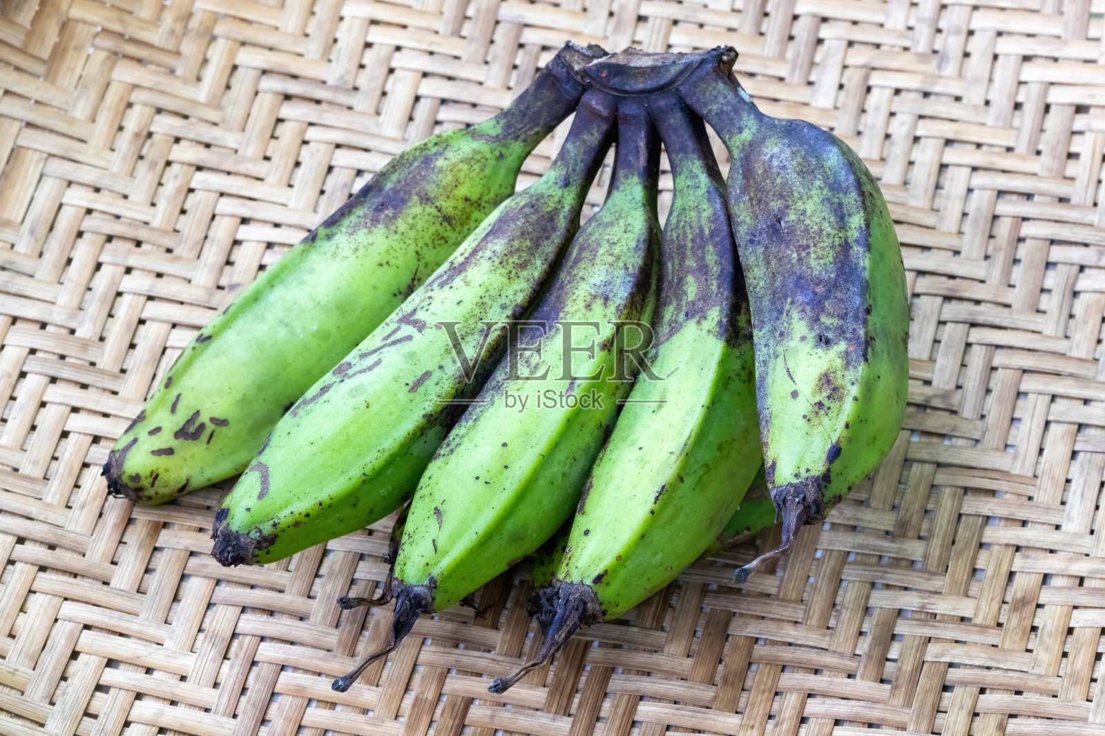 一束生香蕉或绿香蕉在柳条篮子的背景。照片摄影图片