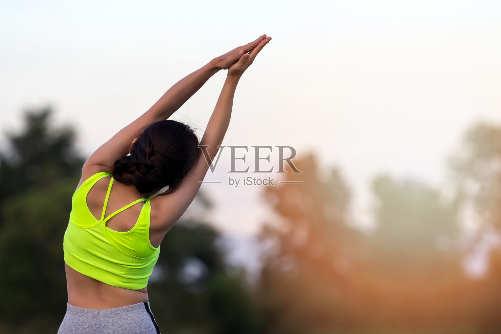 在夕阳下对着树做瑜伽的女人的后视图照片摄影图片
