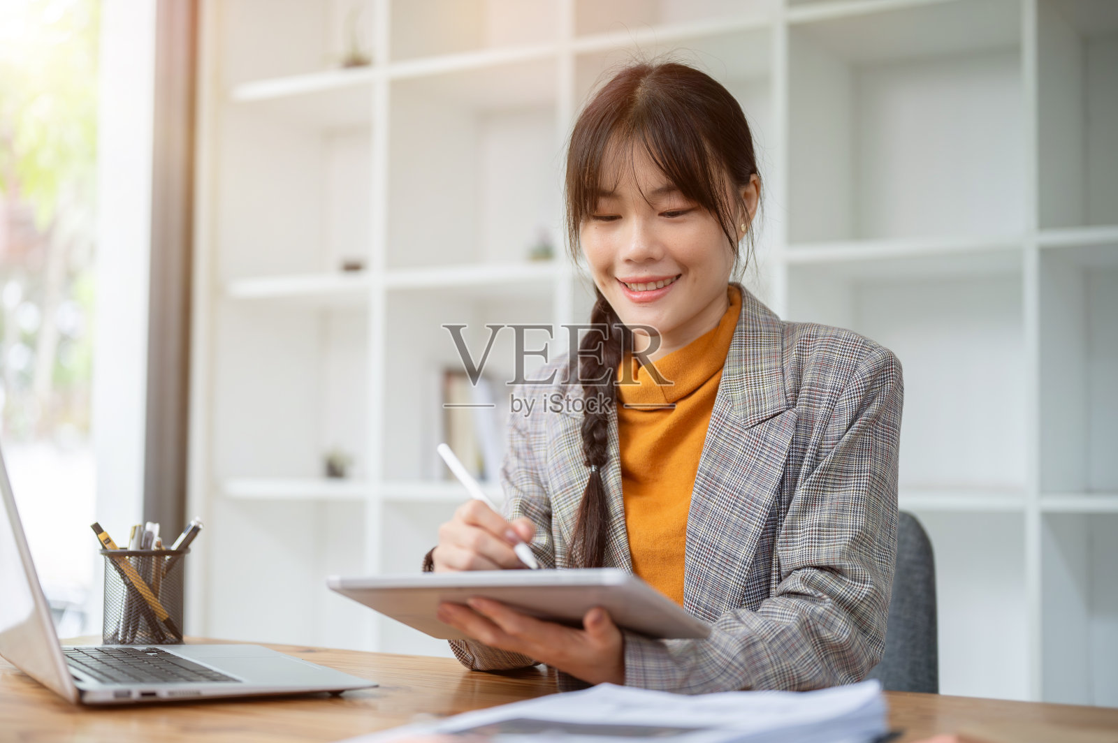 一位迷人、积极的亚洲女商人正在办公室的办公桌前使用一台数字平板电脑。照片摄影图片