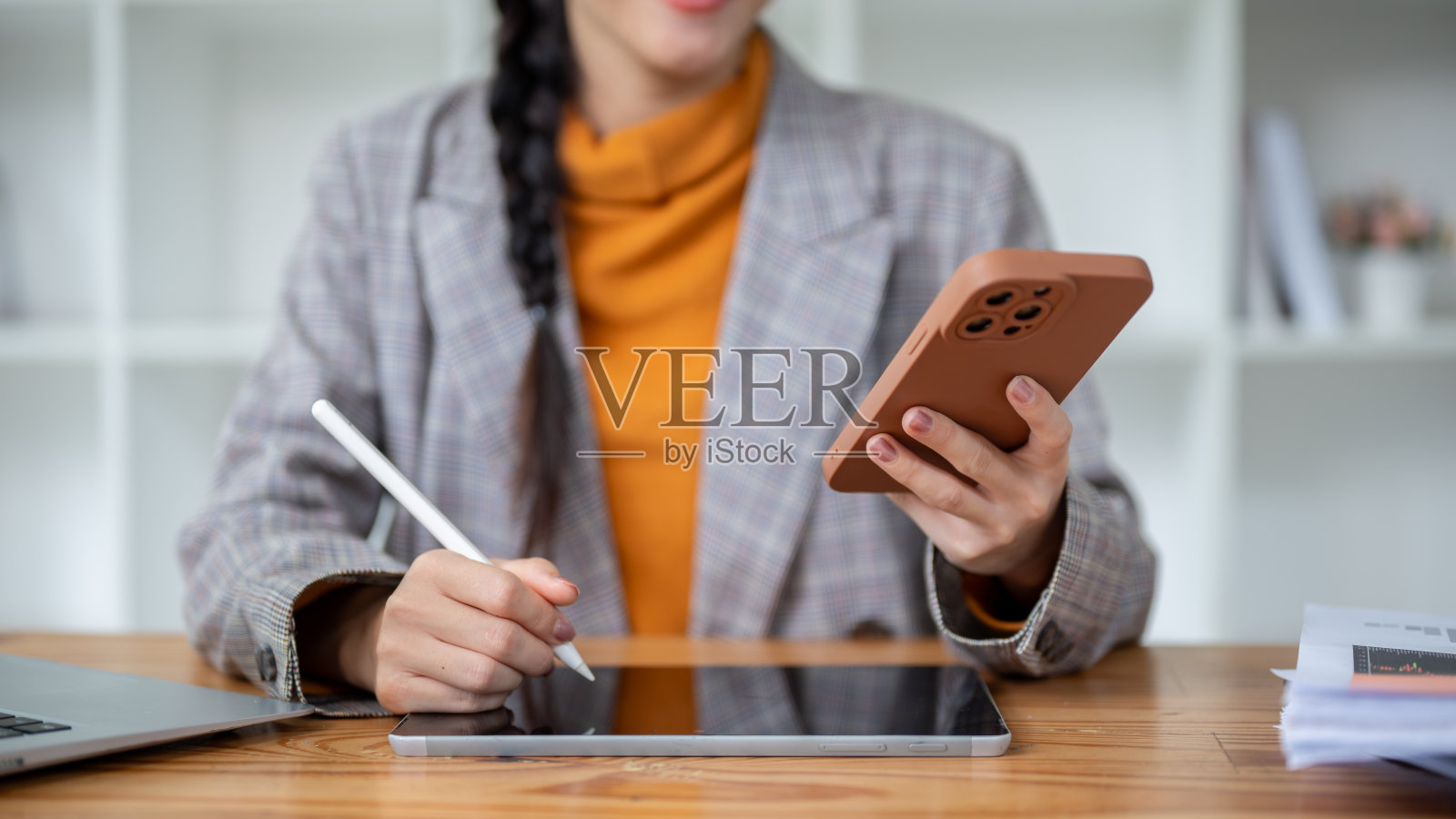 图为一名亚洲女商人正在用智能手机在平板电脑上写字。照片摄影图片