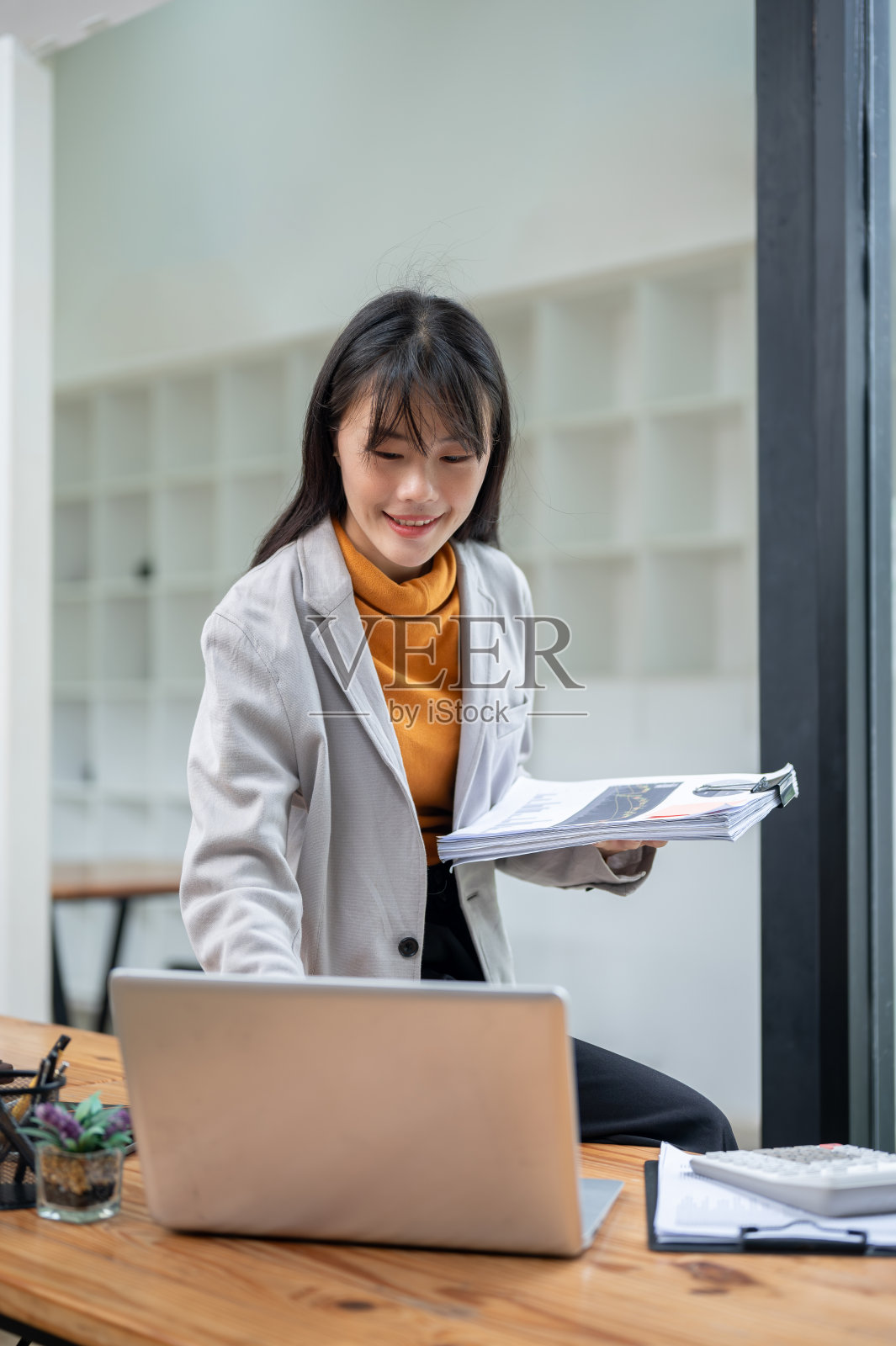 一位漂亮的亚洲女商人靠在桌子上，用她的笔记本电脑工作。照片摄影图片
