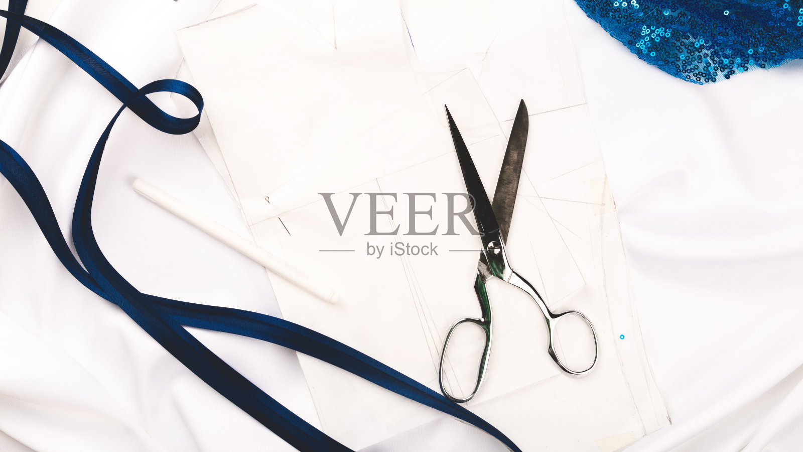 裁剪的概念。美丽的蓝色亮片织物与缝纫线和线轴在一个白色的背景。俯视图，平铺。照片摄影图片