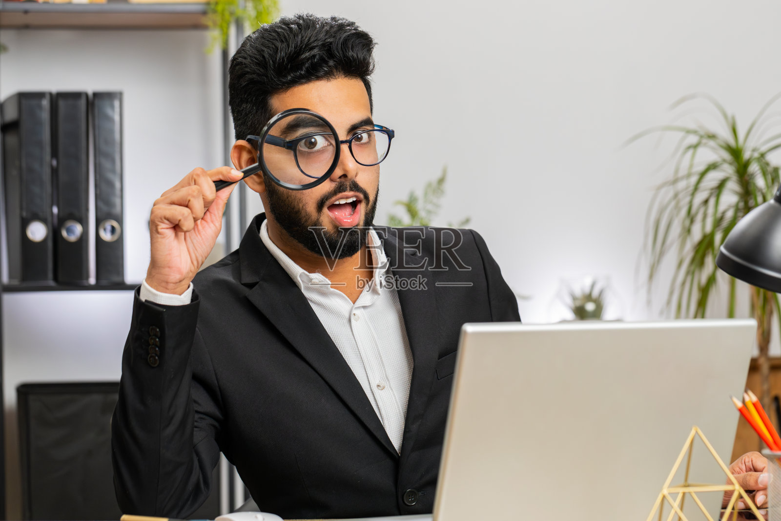 商人拿着放大镜靠近脸，用放大的大眼睛看着，搜索着，分析着照片摄影图片