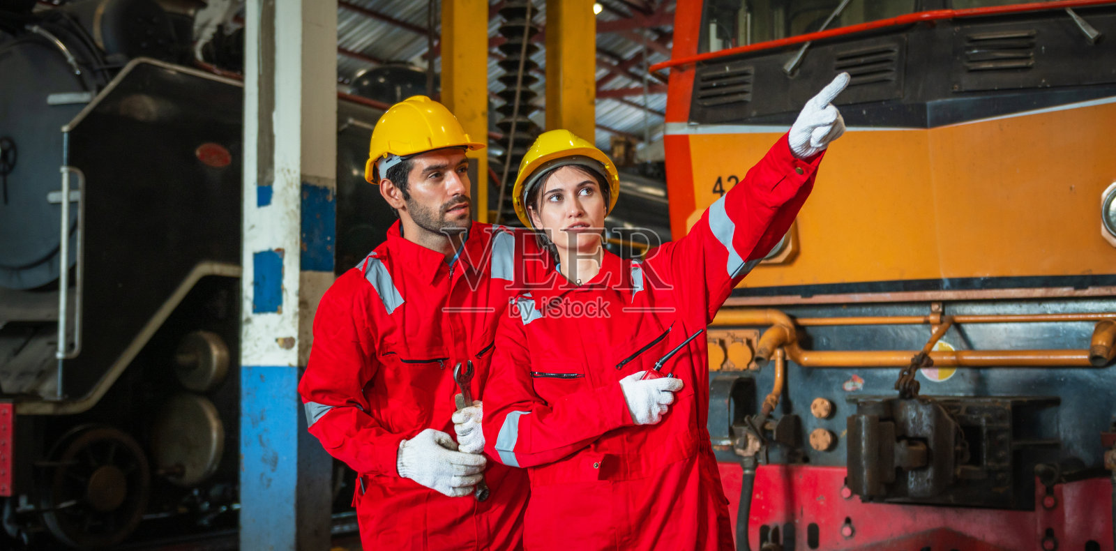 两个穿着红黄相间安全装备的工人指着一列火车照片摄影图片