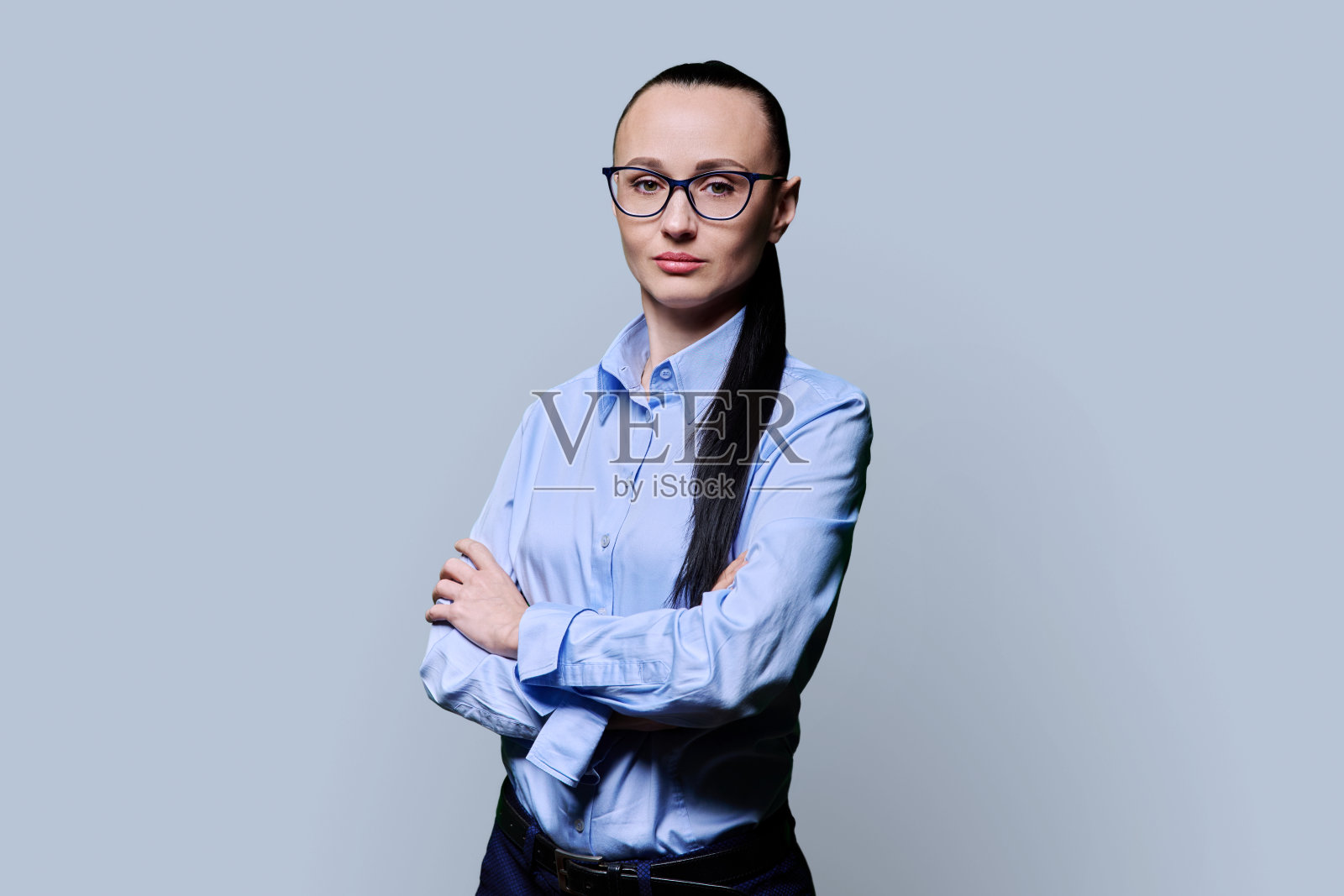 在灰色背景上，30多岁的商界女性双臂交叉的肖像照片摄影图片
