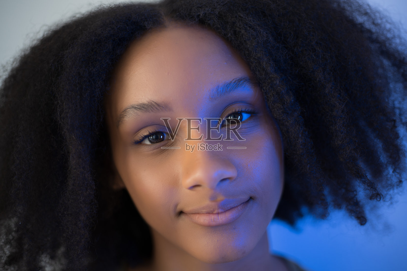在自然光和蓝光的照射下，一头卷发的年轻非裔美国妇女的特写肖像照片摄影图片